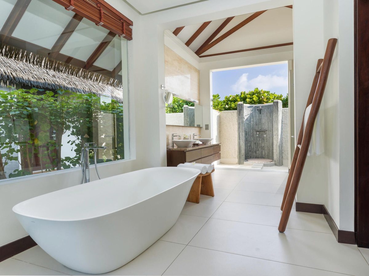 A villa bathroom with a freestanding tub beside a glass wall, tropical greenery visible outside.