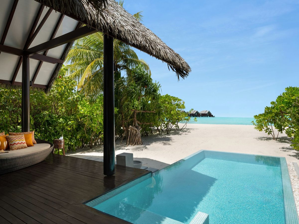 A small private plunge pool on a timber deck under a thatched shade, with the beach and sea just beyond.