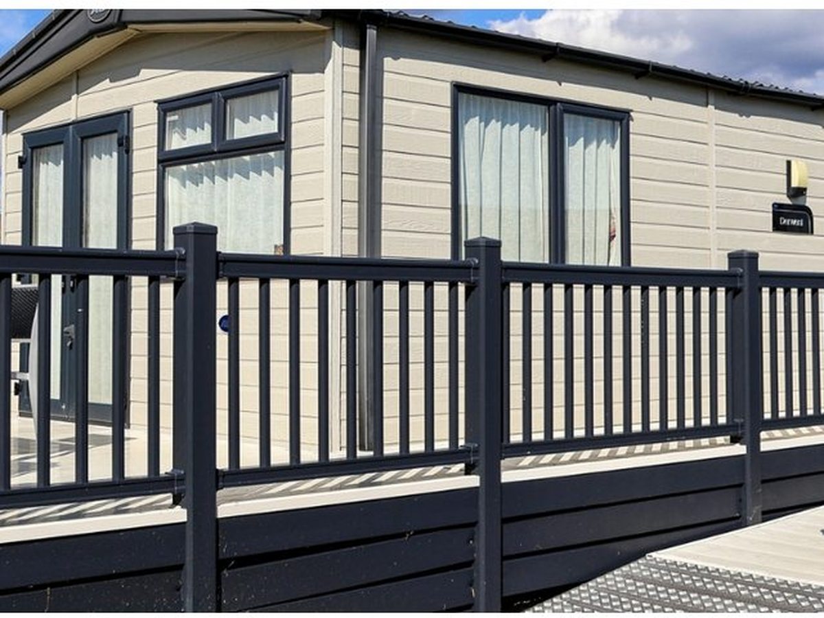 A cream holiday caravan with grey trim and a raised deck with dark railings under a blue sky.