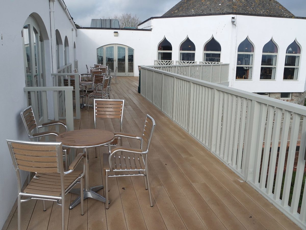 A decked terrace with metal cafe tables and chairs beside the octagonal leisure building with pointed-arch windows.