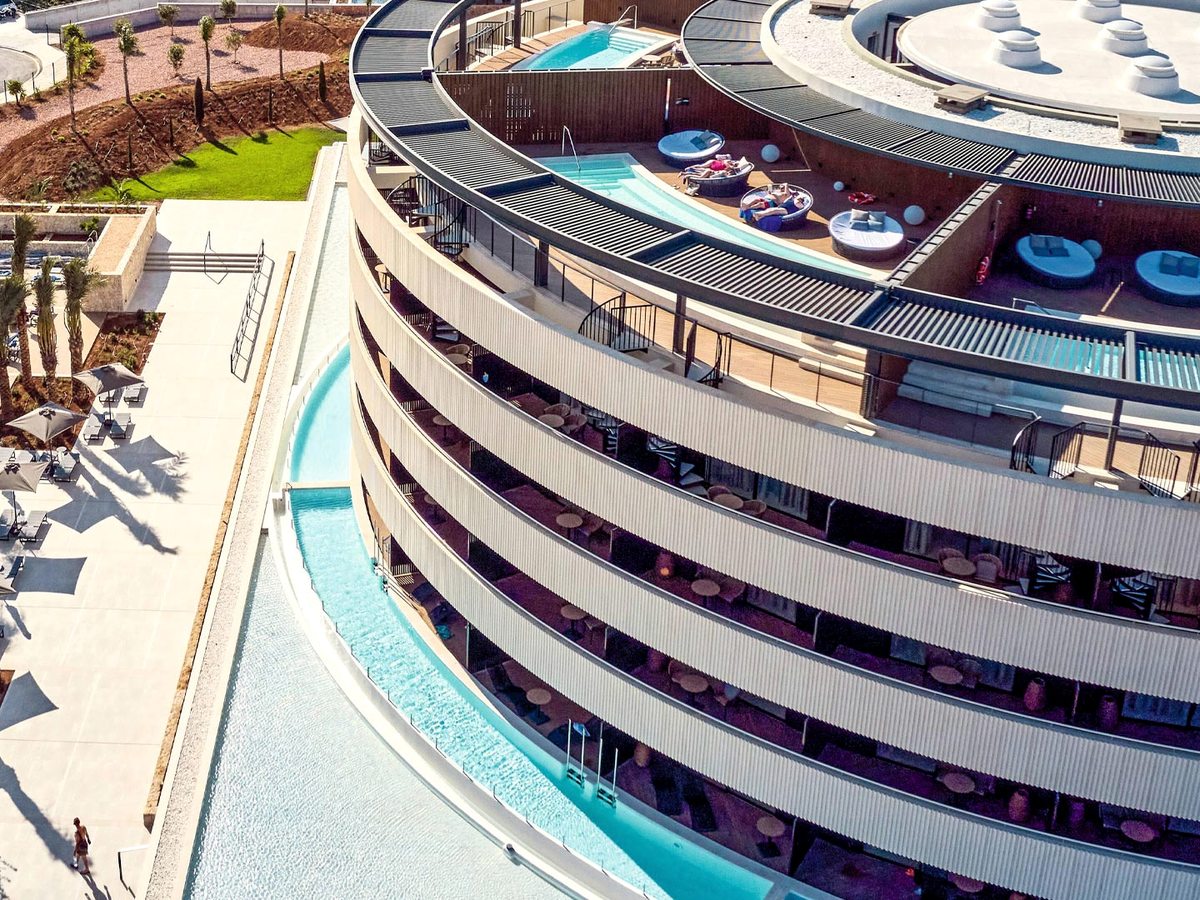 Aerial view of the resort's curved tiered building, with narrow swim-up pools wrapping the lower floors and round daybeds on the roof terraces.
