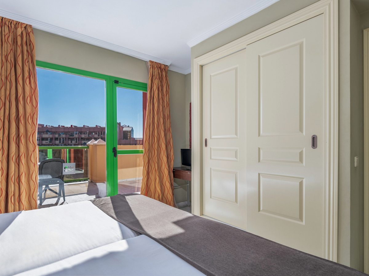 A double bedroom with a built-in sliding-door wardrobe, patterned curtains and a glazed door onto a furnished balcony.