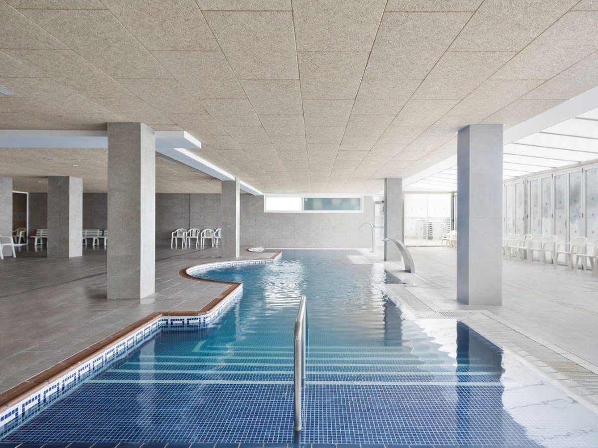 A long indoor pool with a blue-tiled surround in a concrete-walled hall.