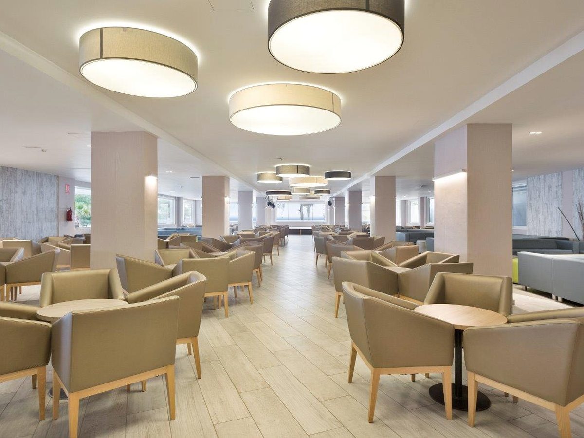 A lobby lounge with armchairs and low tables under round ceiling lights.