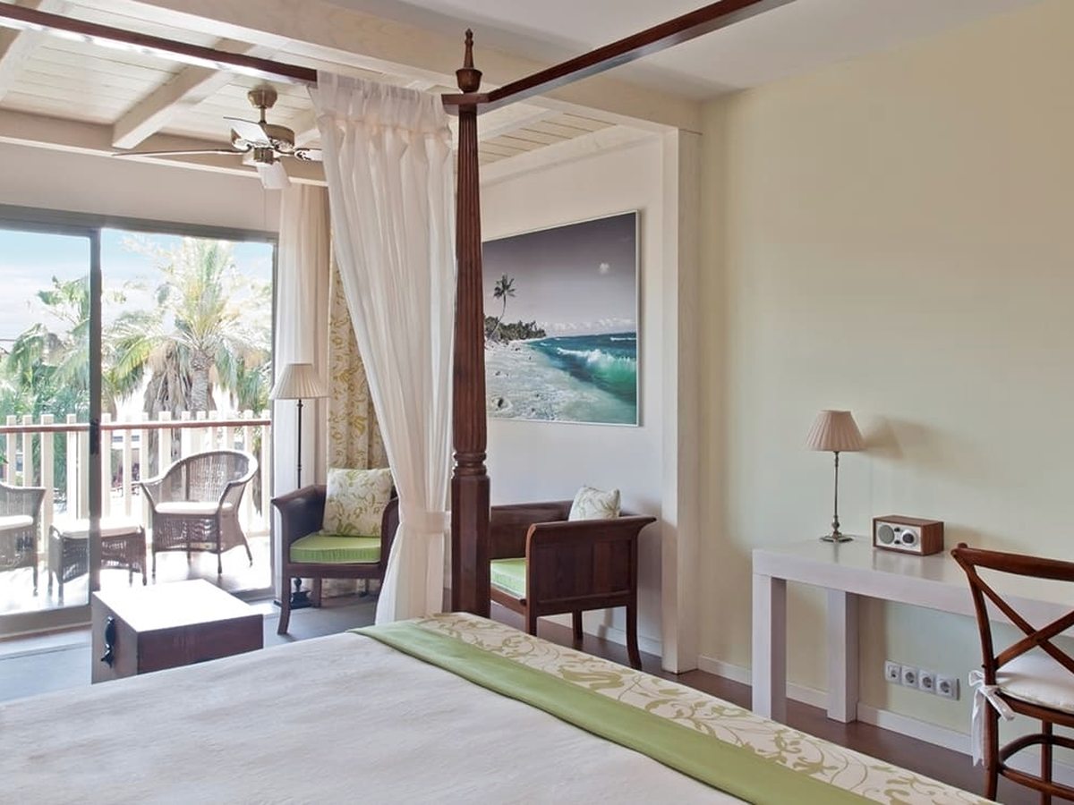 A Club San Juan room with a dark four-poster bed, a private terrace with wicker chairs and a ceiling fan overhead.