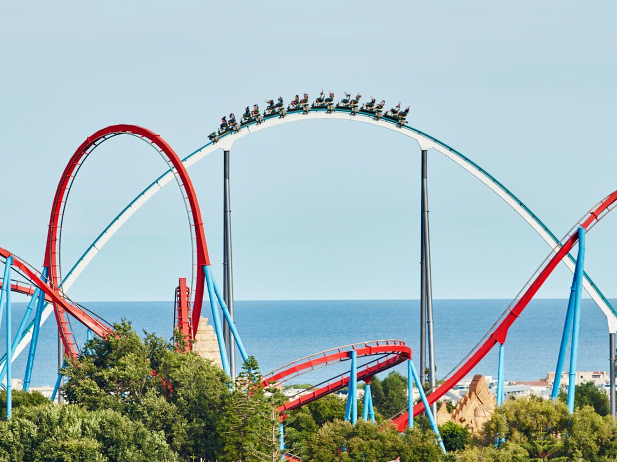 Riders near the top of a tall looping steel rollercoaster against a clear sky, the sea on the horizon at PortAventura Park.