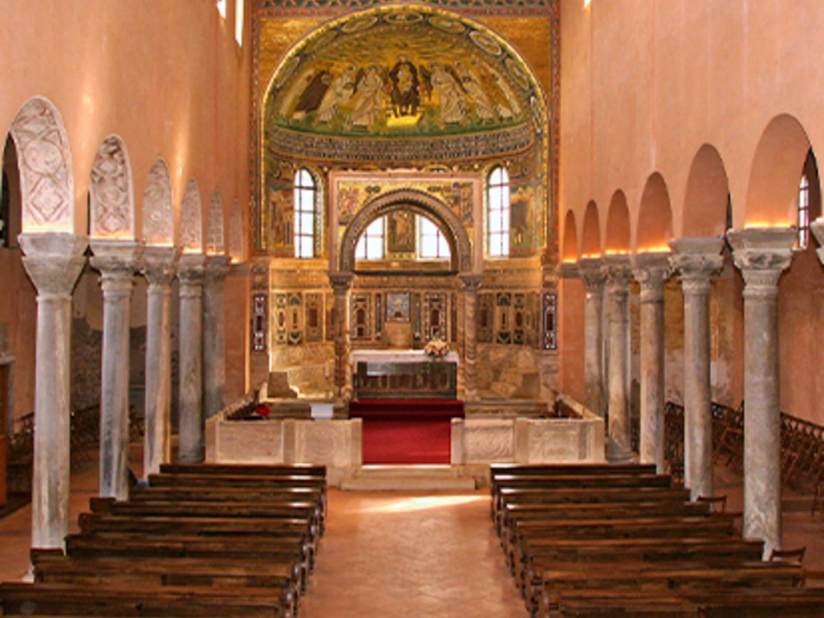The interior of a Byzantine basilica with marble columns, arches and a gold mosaic filling the apse above the altar.