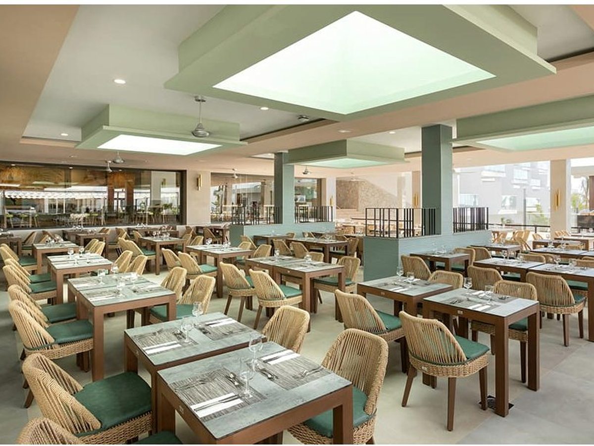 Interior of the main buffet restaurant with rows of set tables and green chairs under a bright ceiling, live cooking stations behind.