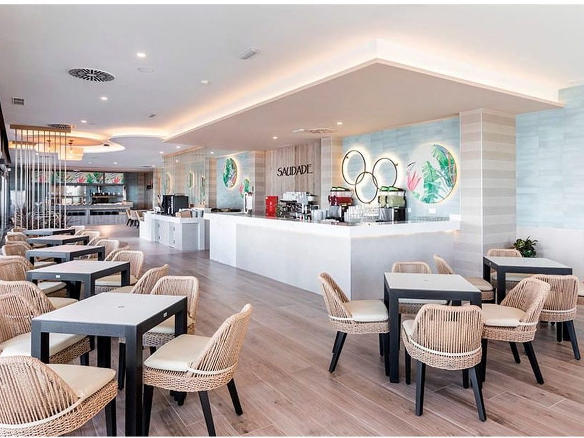 Café-bar with a pale service counter, coffee machines and woven chairs on a light wood floor.