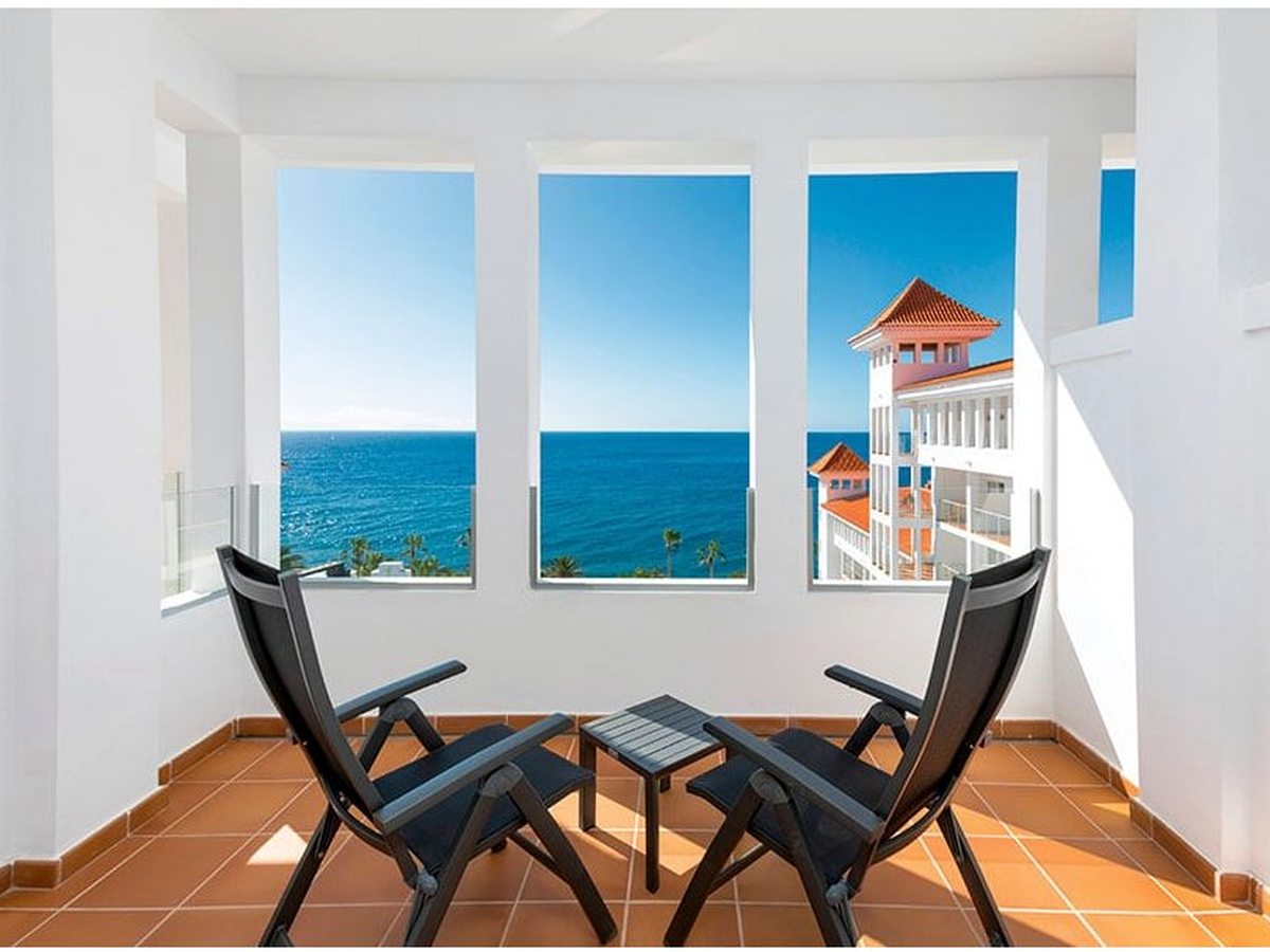 Enclosed room balcony with terracotta floor tiles, two folding chairs and a small table, looking over the Atlantic to the hotel's terracotta-roofed wing.