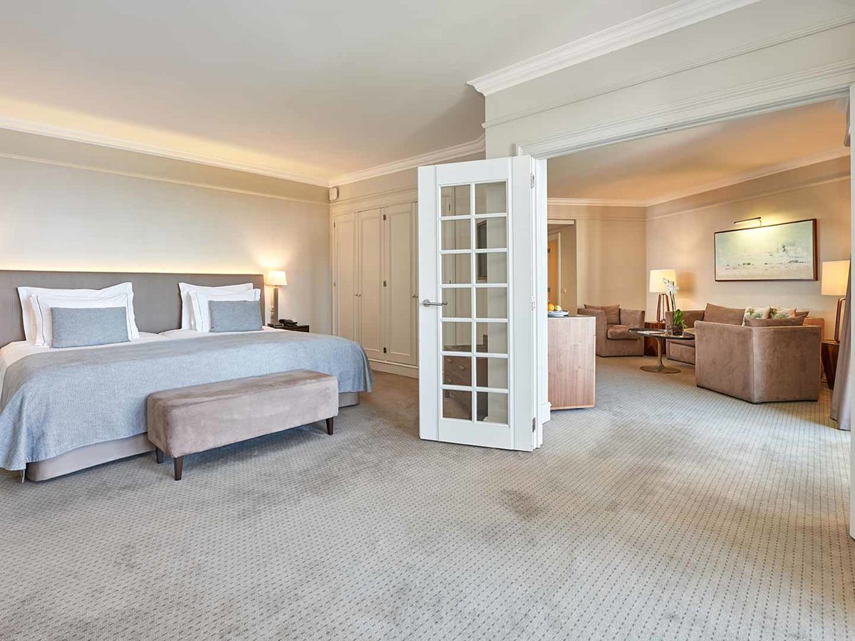 A suite with a king bed on one side and folding glass doors opening to a separate lounge with sofas and framed artwork.