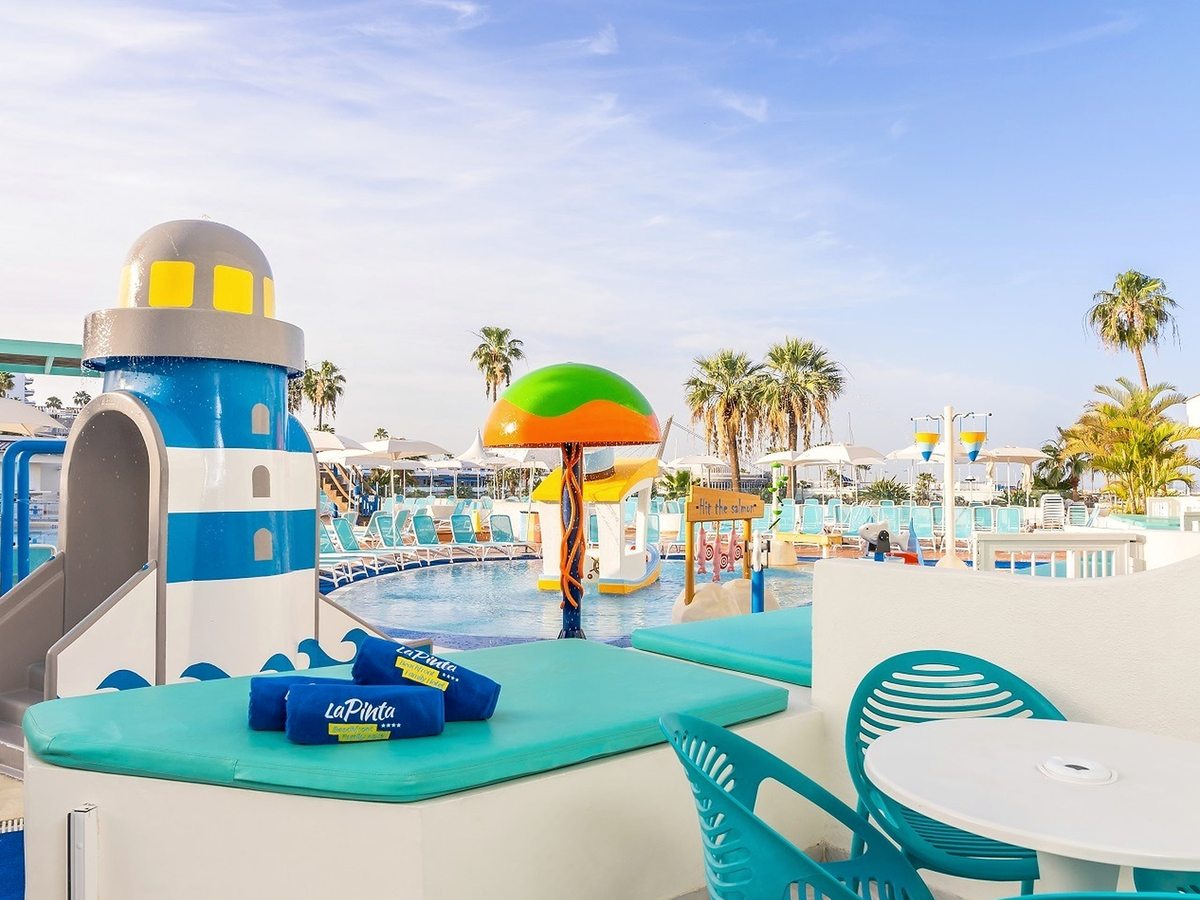 A shallow children's splash area with a lighthouse feature and water toys beside the pool deck.