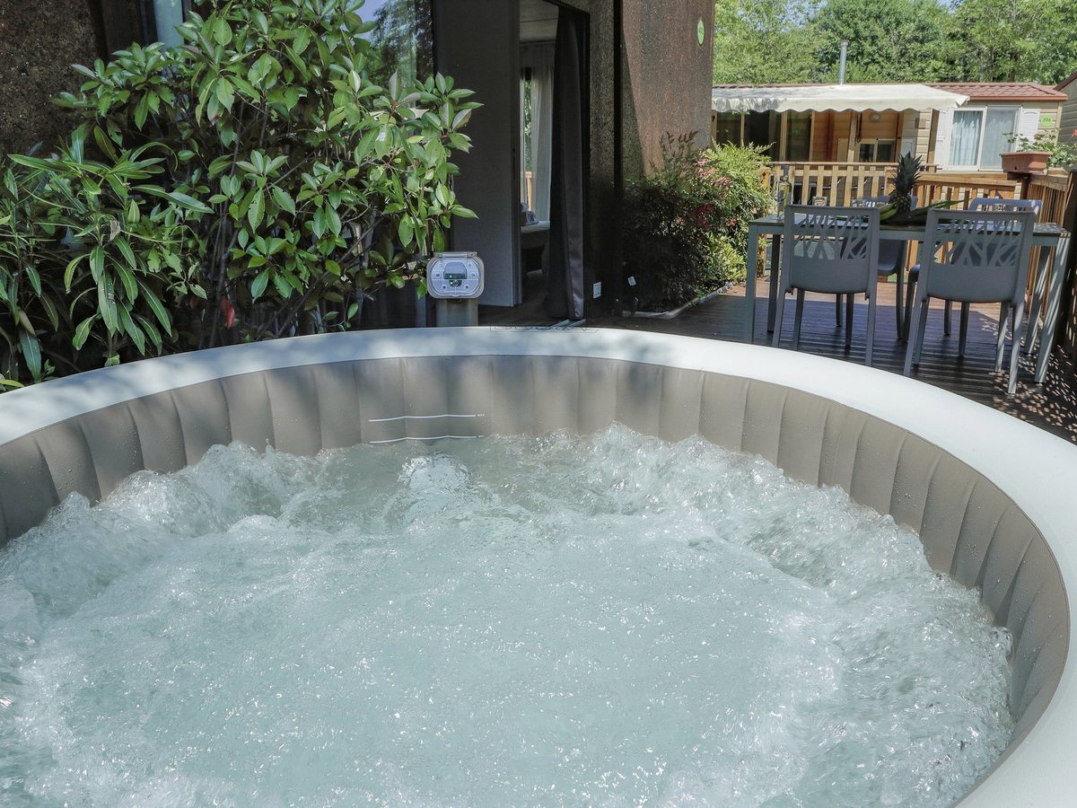 A round whirlpool tub with bubbling water on a covered wooden deck surrounded by greenery.