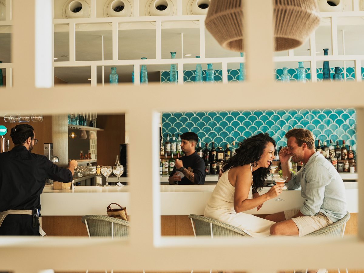 A bar with a turquoise-tiled counter, taps and stools, with guests being served drinks.