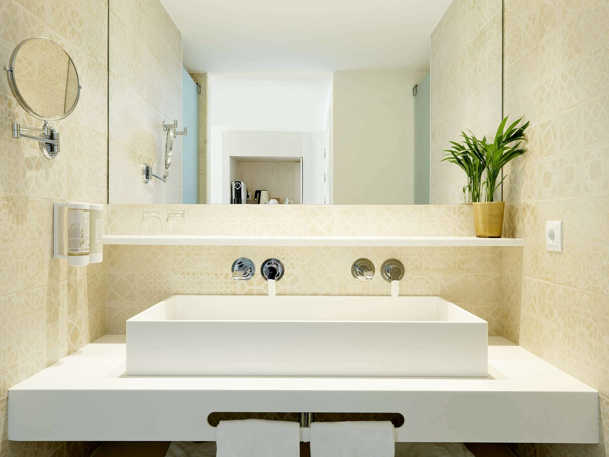 A bright bathroom with a rectangular basin on a cream-tiled vanity, a wide mirror and a magnifying mirror.