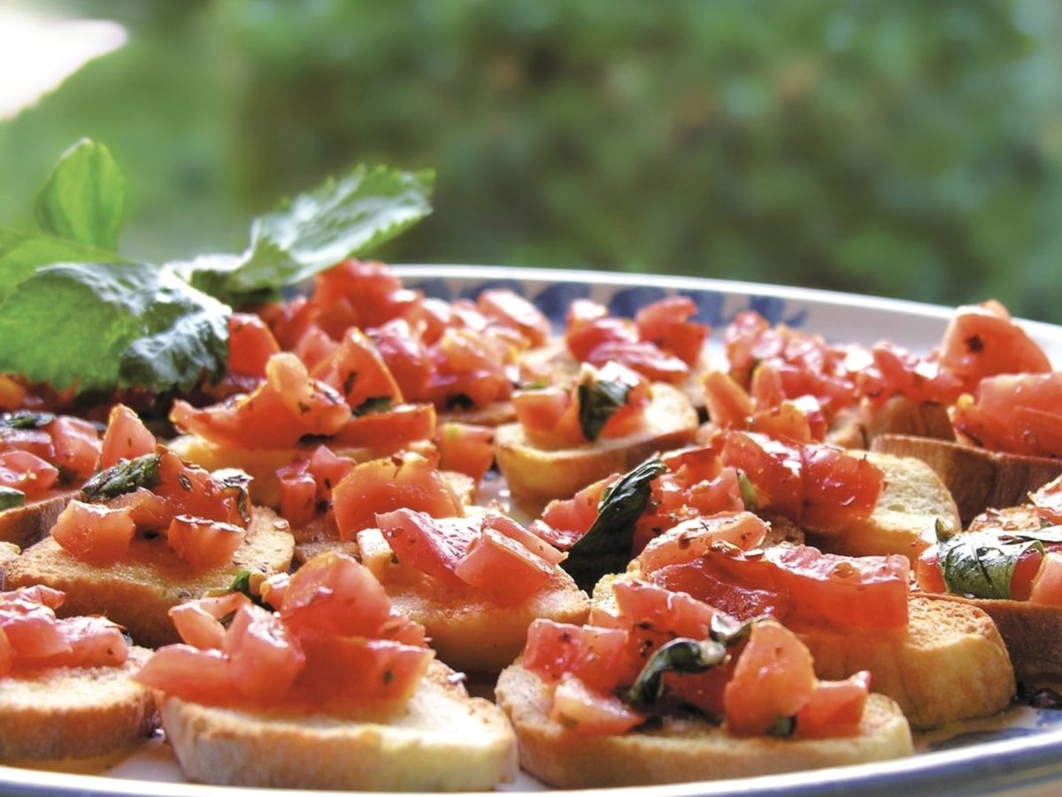 A platter of tomato bruschetta, toasted bread topped with diced tomato and basil, on a metal serving tray.