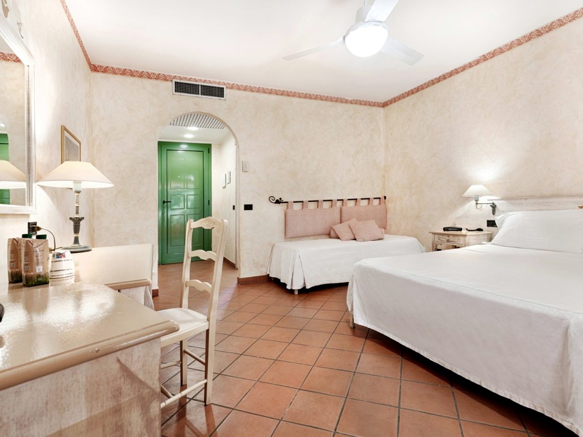 A family room with a double bed and a single child's bed alongside, a writing desk and a terracotta-tiled floor.