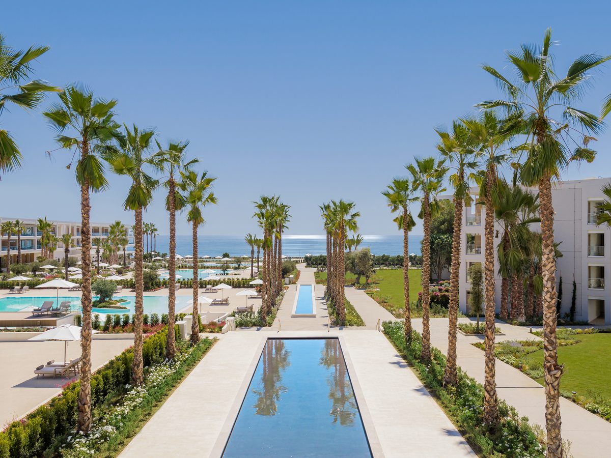 The central boulevard at Ikos Andalusia, a long reflecting pool between rows of palms, with the pools to one side and the sea at the far end.