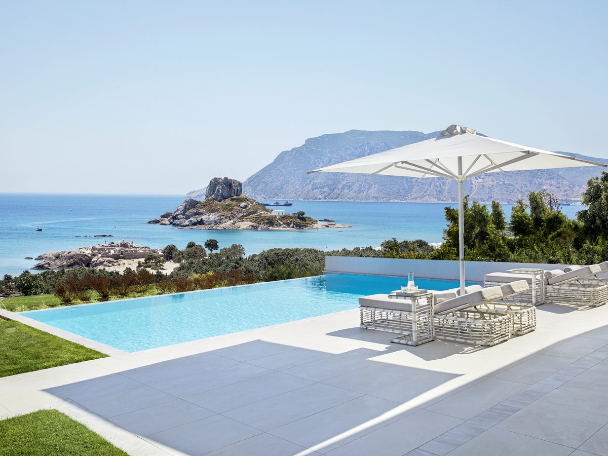 The private pool of a Deluxe Two Bedroom Bungalow Suite, with a parasol and sun loungers on the terrace and the Kastri islet beyond.