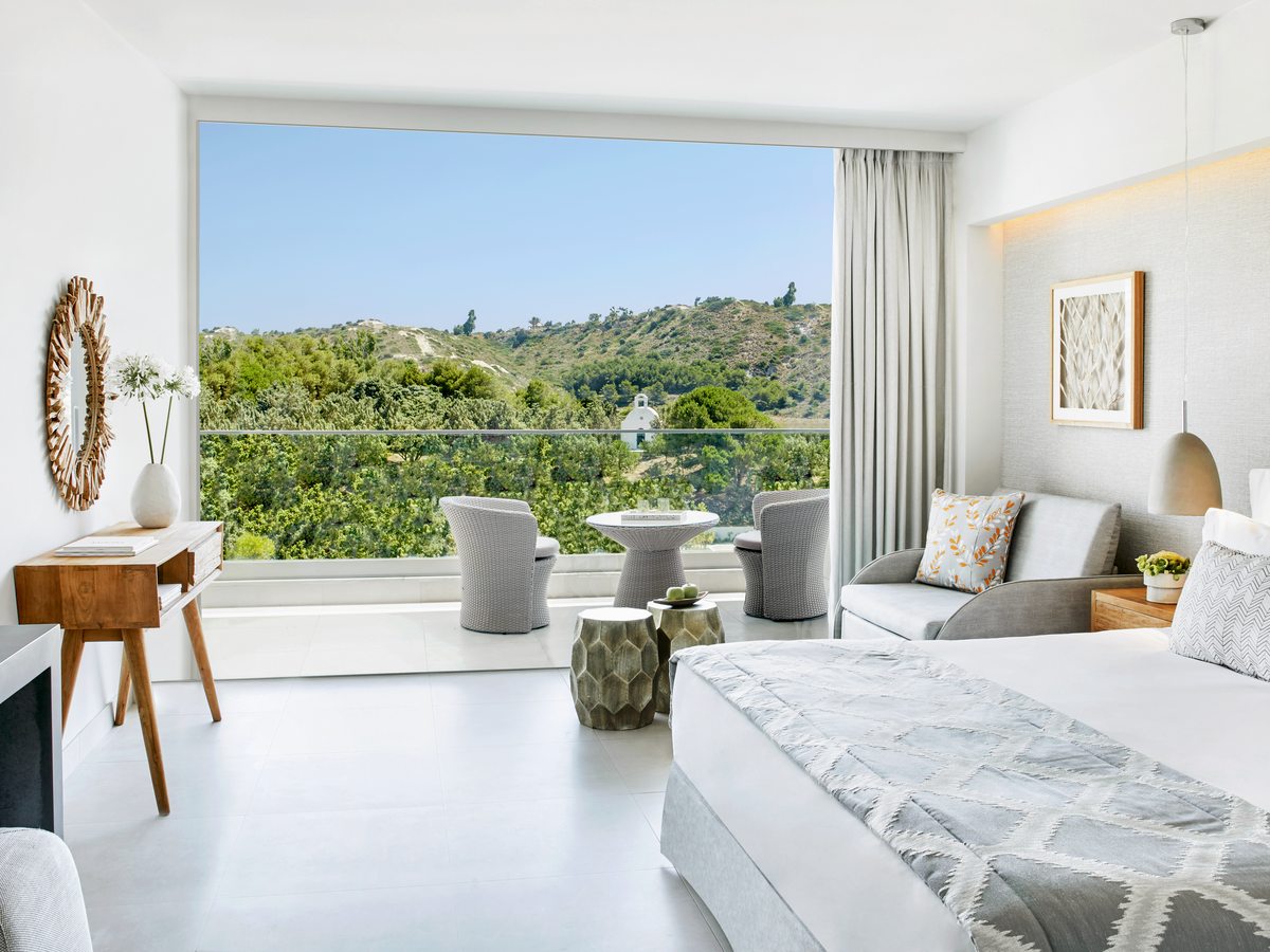 A Double Room with a king bed, a writing desk and a wide window onto the gardens and the hills behind the resort.