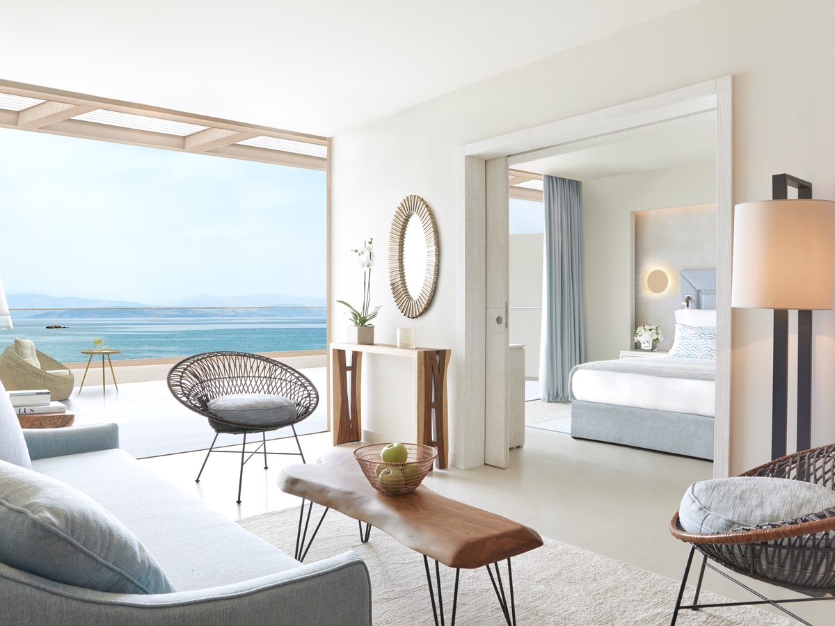 Suite living room with a sofa and armchairs, an open doorway through to the bedroom and a terrace beyond.