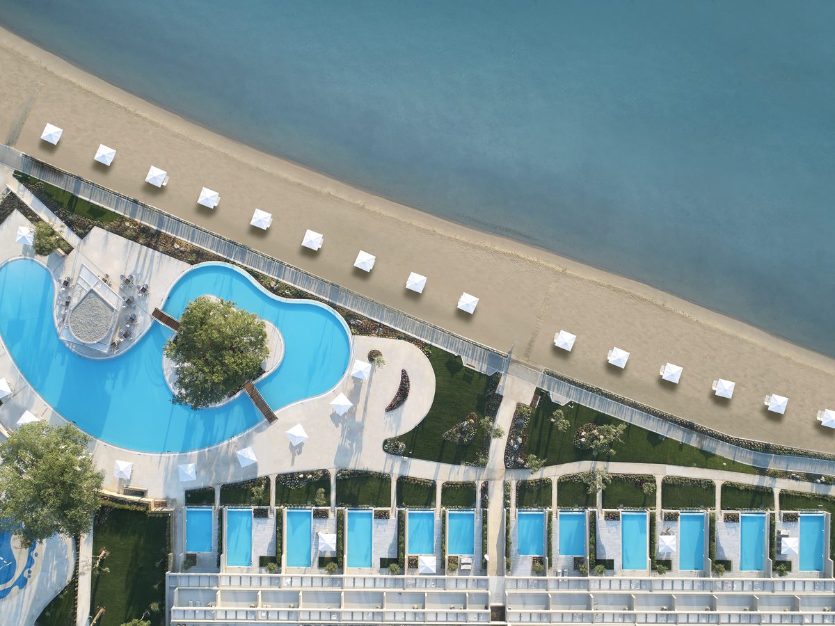 Aerial view of a large free-form pool with a planted island, sun loungers along the surround and the sand beyond.