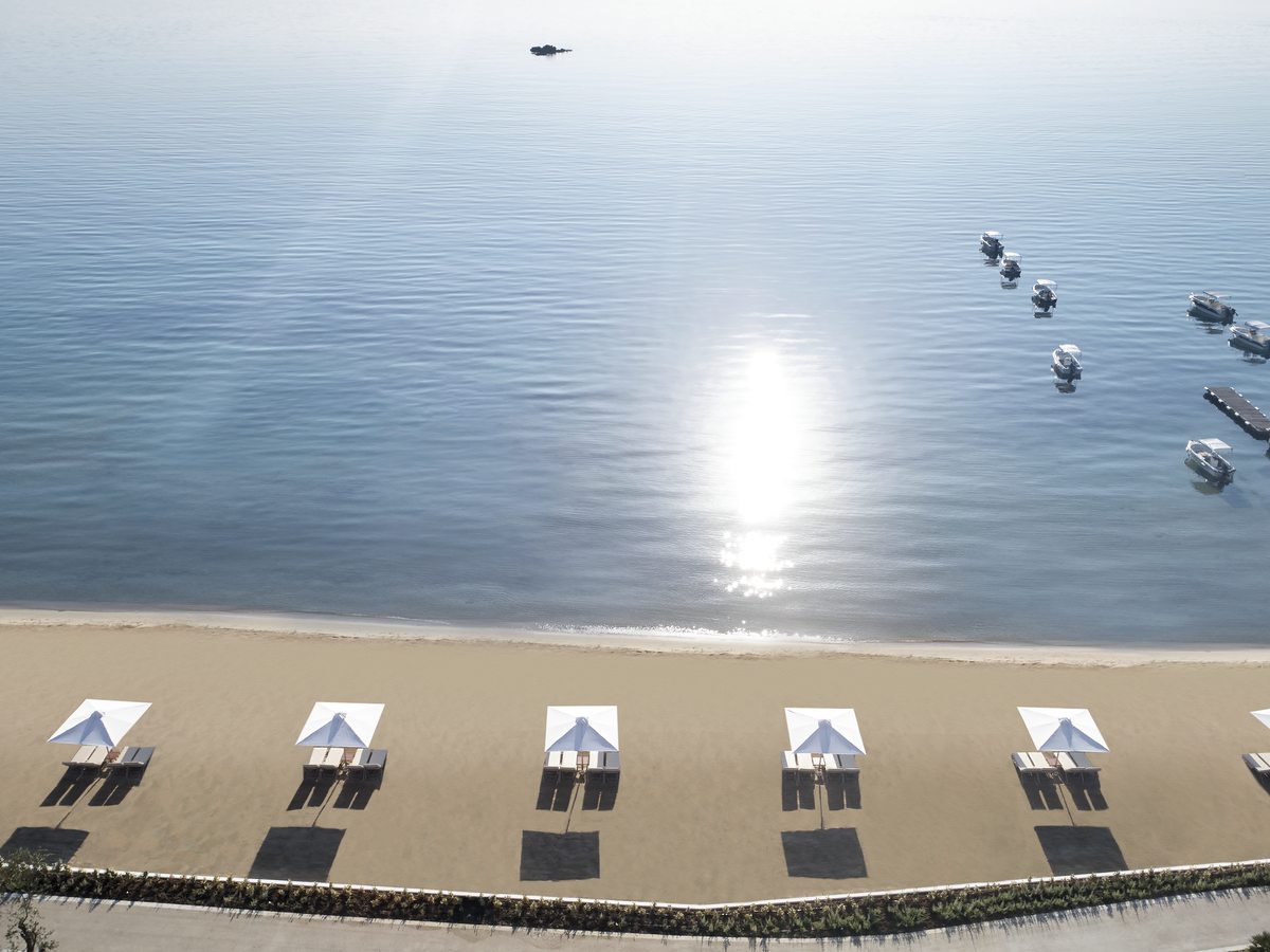 Pairs of sunbeds and parasols spaced along the sand, with the sun low over flat, calm water.