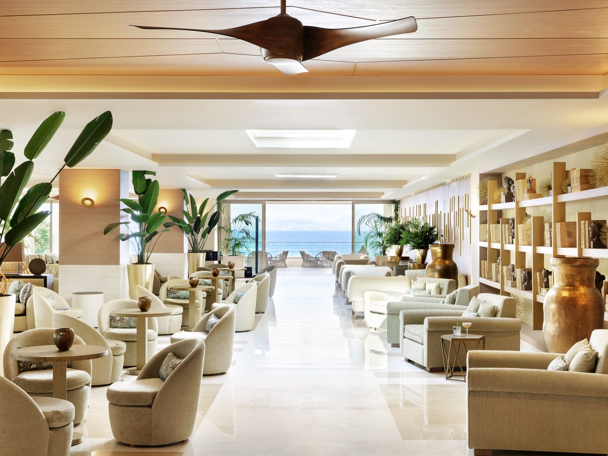 A long lounge of cream armchairs and low tables under a wood-panelled ceiling, opening to the sea at the far end.