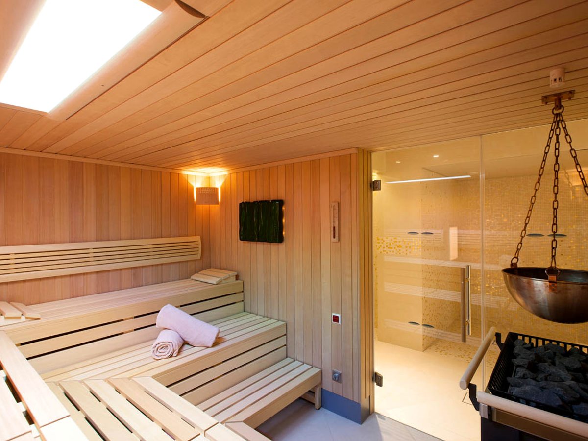 A wooden sauna at an Ikos spa, with tiered benches, a rolled towel and a stove in the corner.