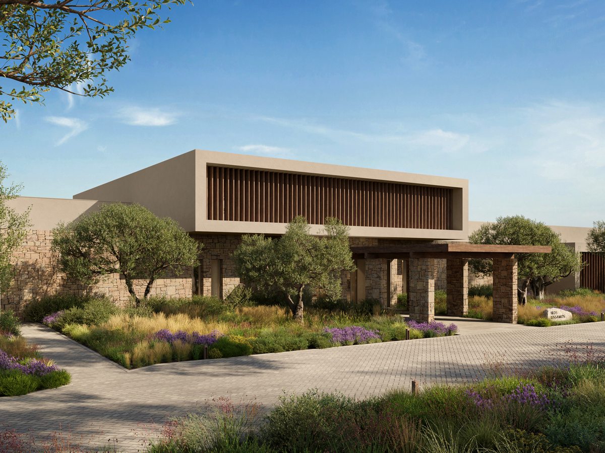 The arrival building at Ikos Kissamos, a low stone-and-timber block behind olive trees and planted beds, with a paved drive in front.