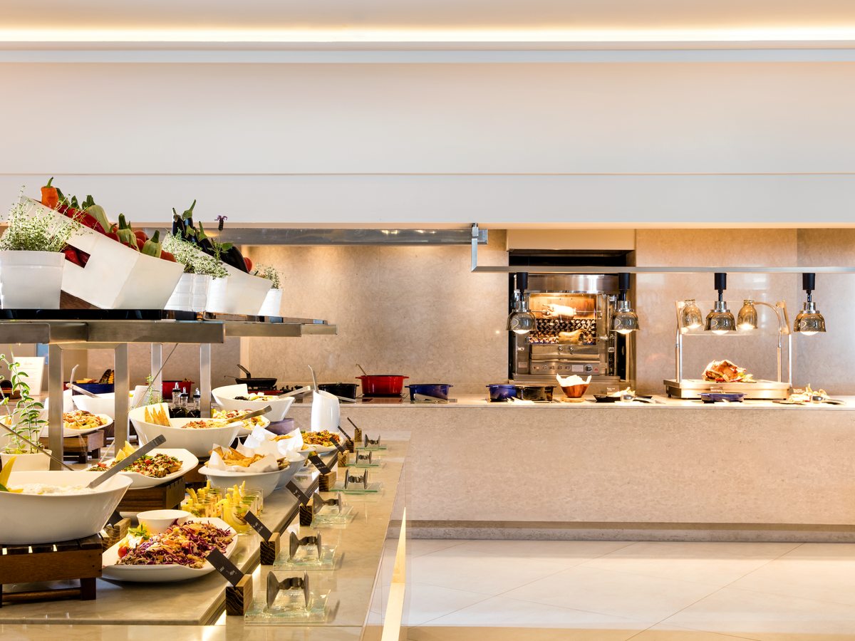 The buffet counter at Flavors, with salad bowls in the foreground, hot dishes under lamps and a chef’s station behind.
