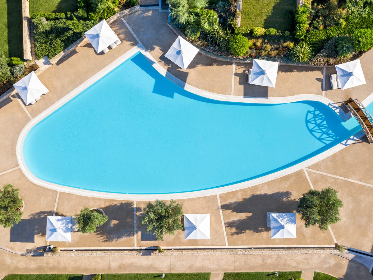 The large lagoon-shaped main pool at Ikos Olivia, ringed with sunbeds, white parasols and planted borders.