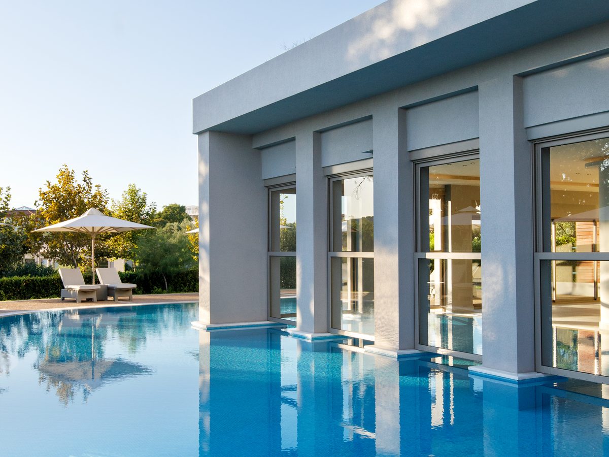 The outdoor pool beside the spa building at Ikos Olivia, with sunbeds and a parasol on the terrace.