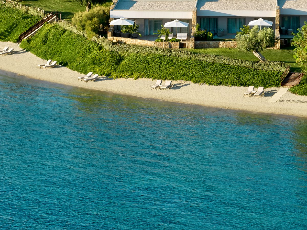 Single-storey bungalows on a low grassy rise just above the sand, with sunbeds set out on the beach below.