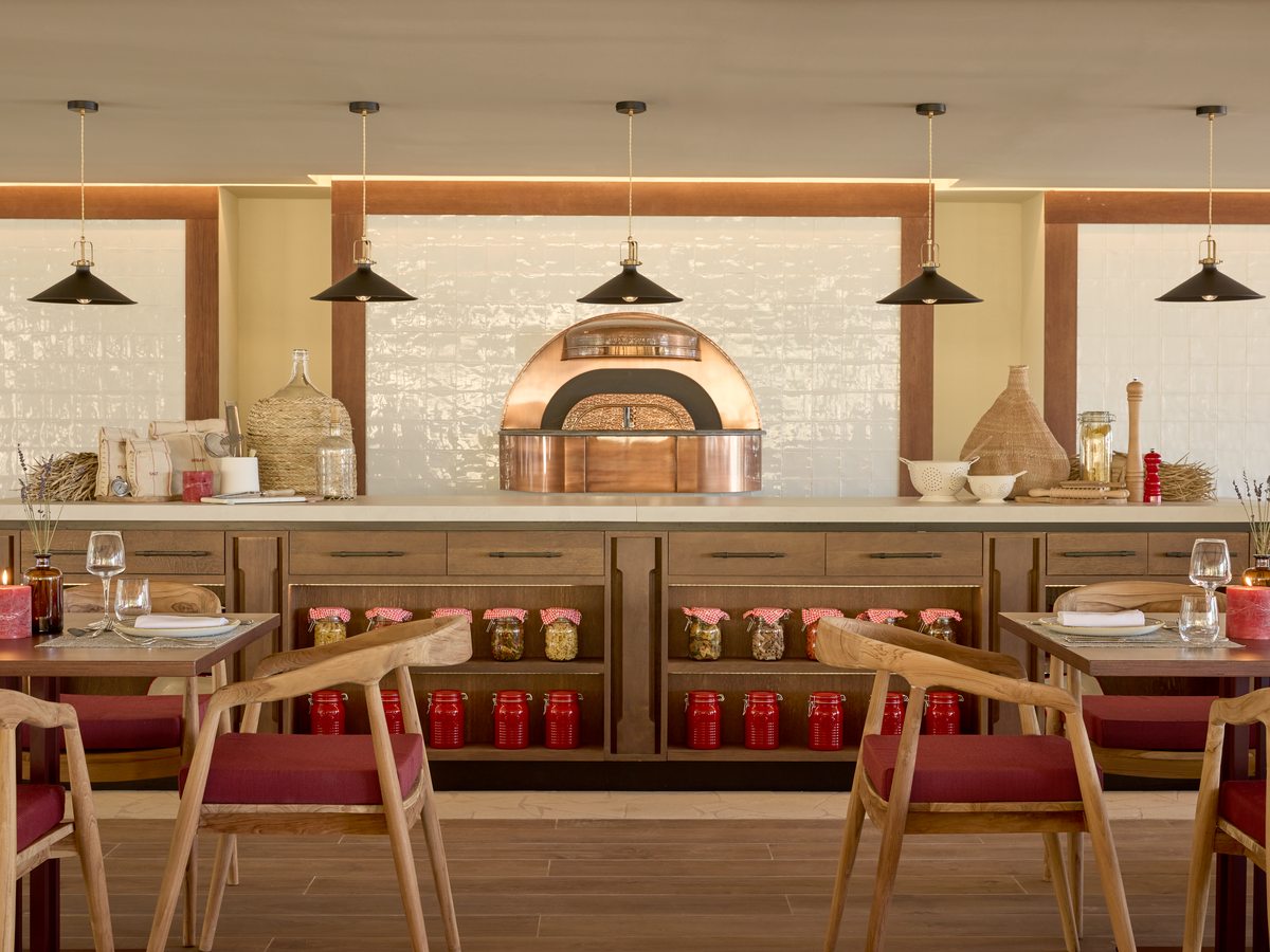 The dining room at Fresco, tables and red-cushioned chairs in front of a copper-domed pizza oven set into a tiled wall.