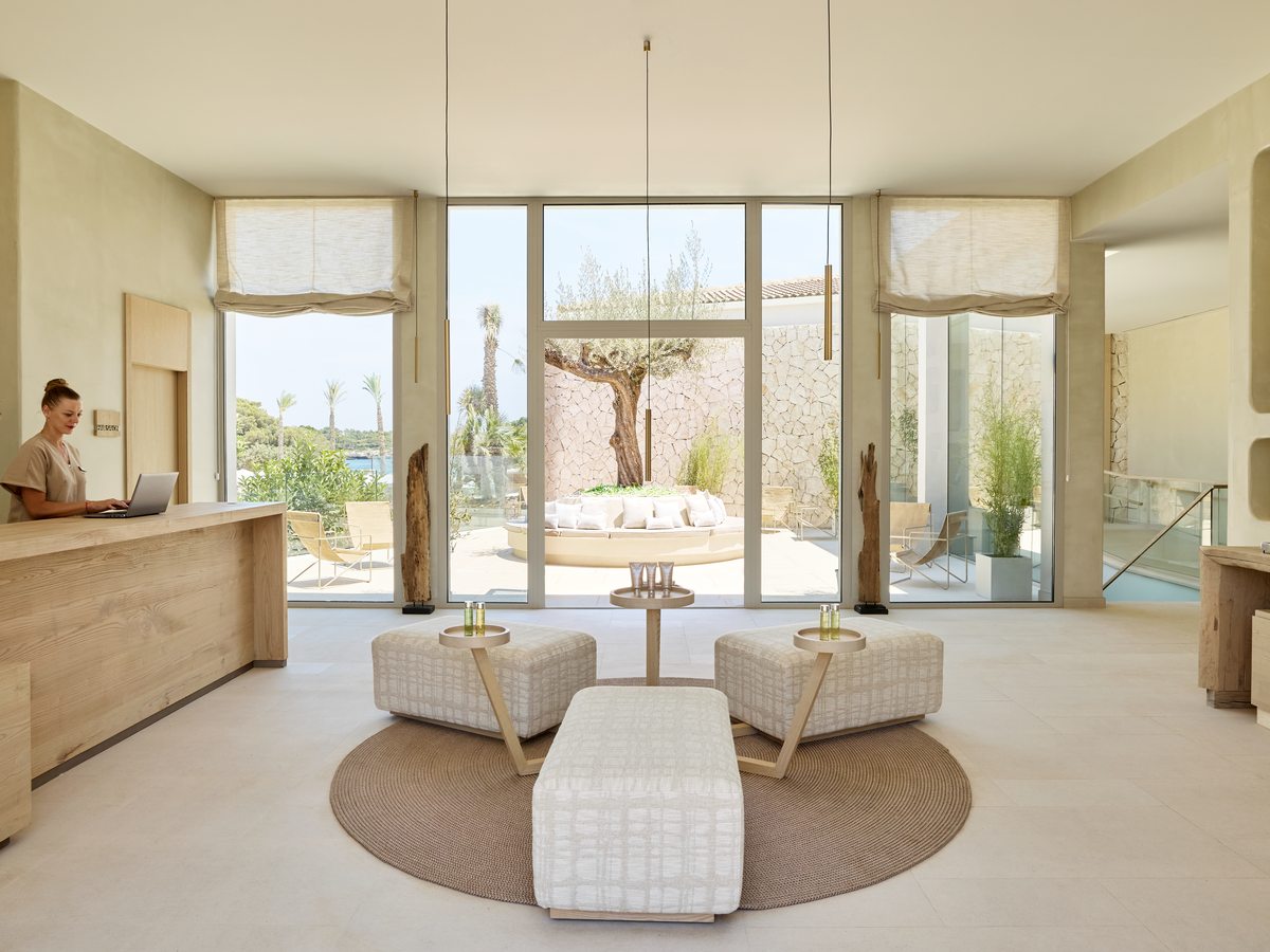 The spa reception, a light room with tall windows, low white seating on a round rug and an olive tree in a planter.