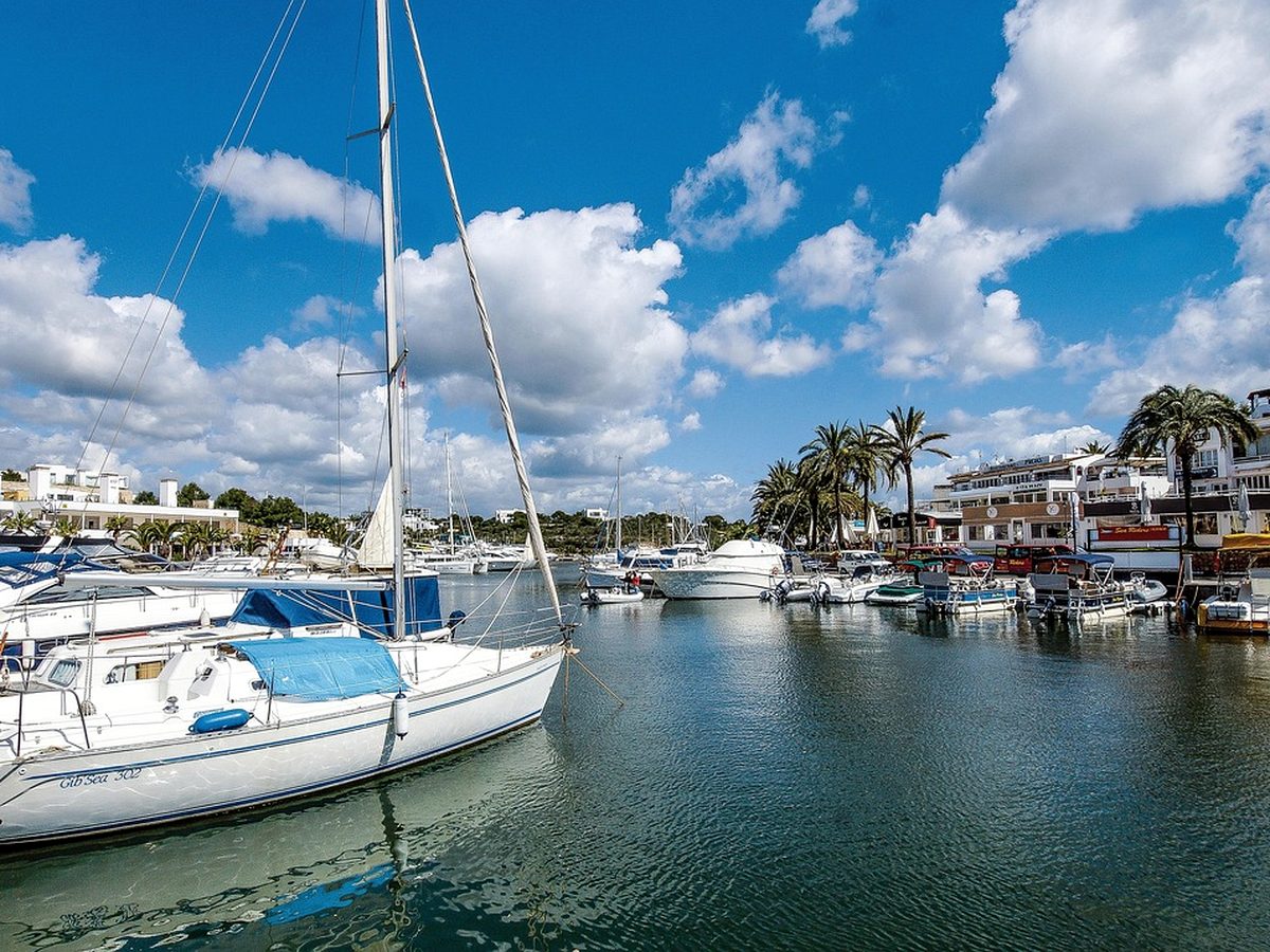 The marina at Cala d'Or, with yachts moored in front of white waterfront buildings and palms.