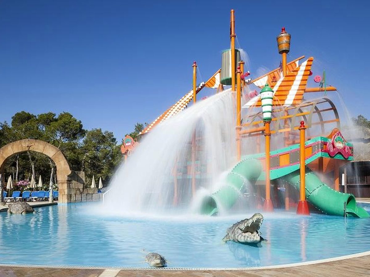 A pirate-ship splash structure with green tube slides and water cannons over a shallow pool.