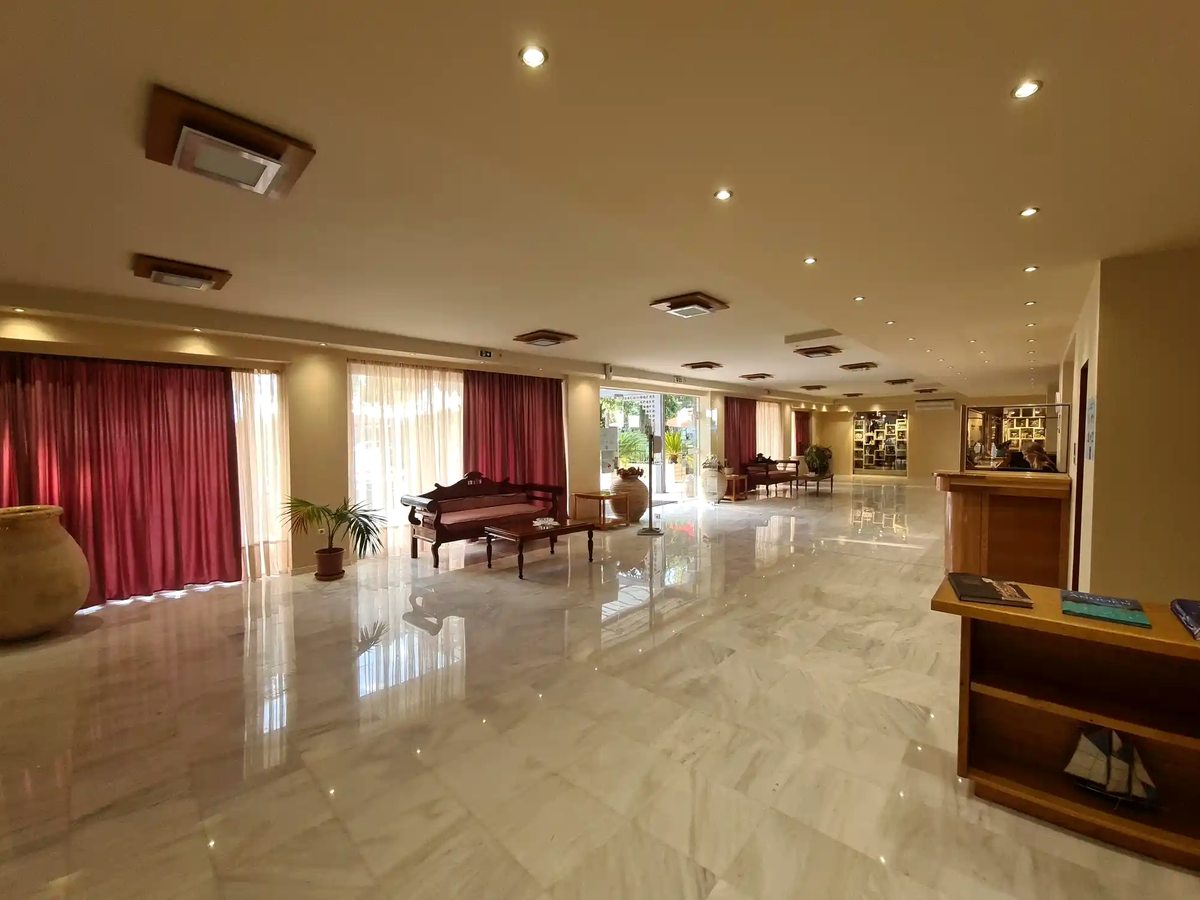 A hotel lobby lounge with a polished marble floor, a grand piano, red drapes and seating.