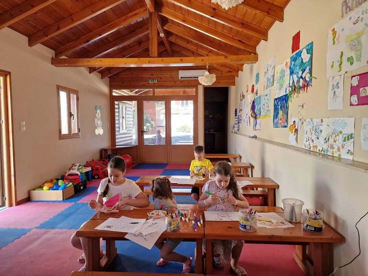A children's club room with a timber ceiling, low tables and chairs, and children's artwork covering the walls.