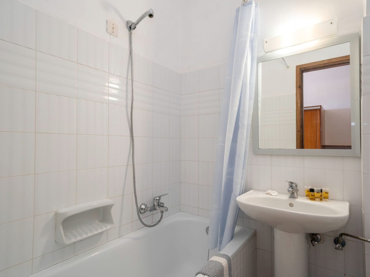 A compact bathroom with a white bathtub, a handheld shower, a curtain and a wall mirror.