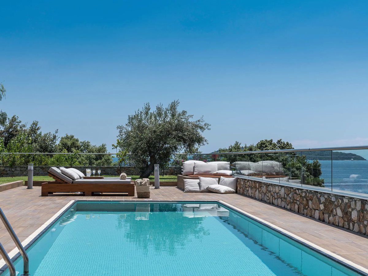 Suite terrace with a private pool, sun loungers and a daybed behind a glass railing above the sea.