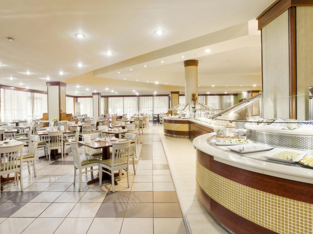 A large indoor buffet restaurant with curved serving counters of salads and hot dishes, tables and chairs and tall curtained windows.