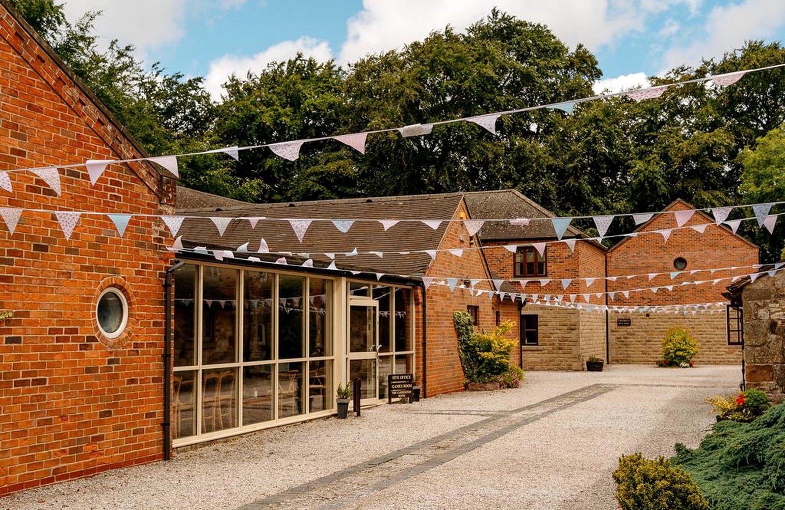 The gravel courtyard at Knockerdown Cottages, with bunting strung between the red-brick converted farm buildings and a glazed room along one side.