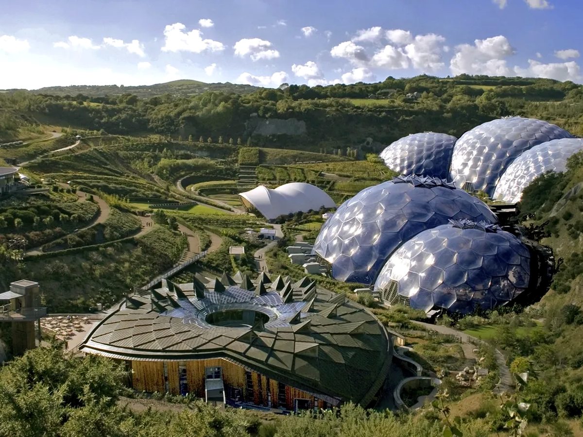 Large white geodesic domes in a landscaped former quarry, with terraced gardens and winding paths around them.