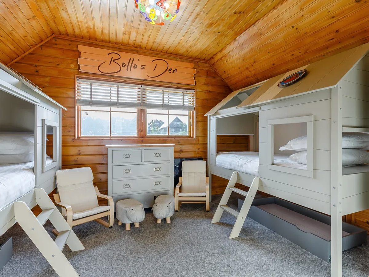 A children's bedroom with white bunk beds, a chest of drawers, two small chairs and a pine-clad ceiling.