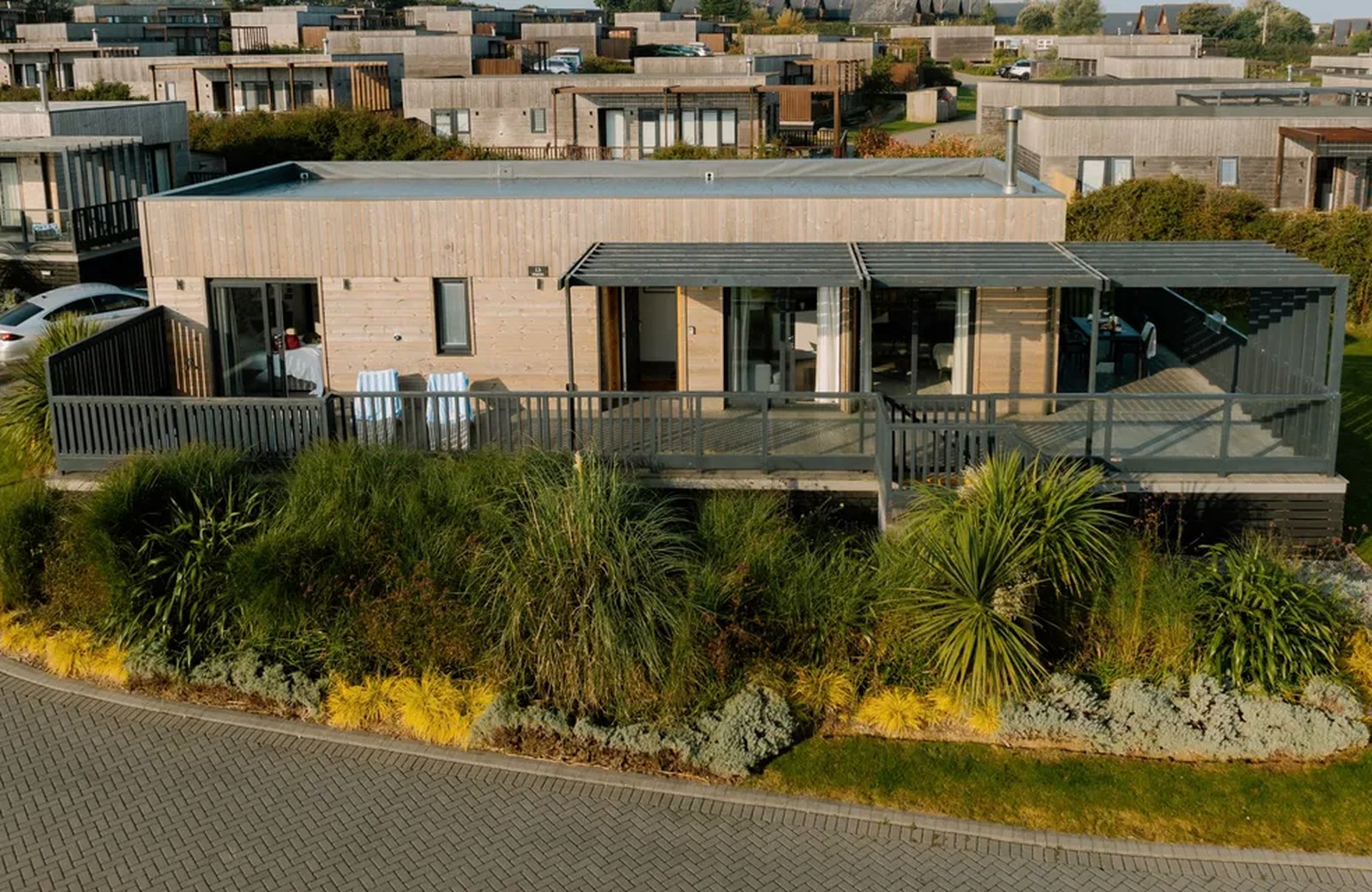 Timber-clad lodges with raised decks and pergolas, set among grasses and cordyline palms on the sloping ground of the park.