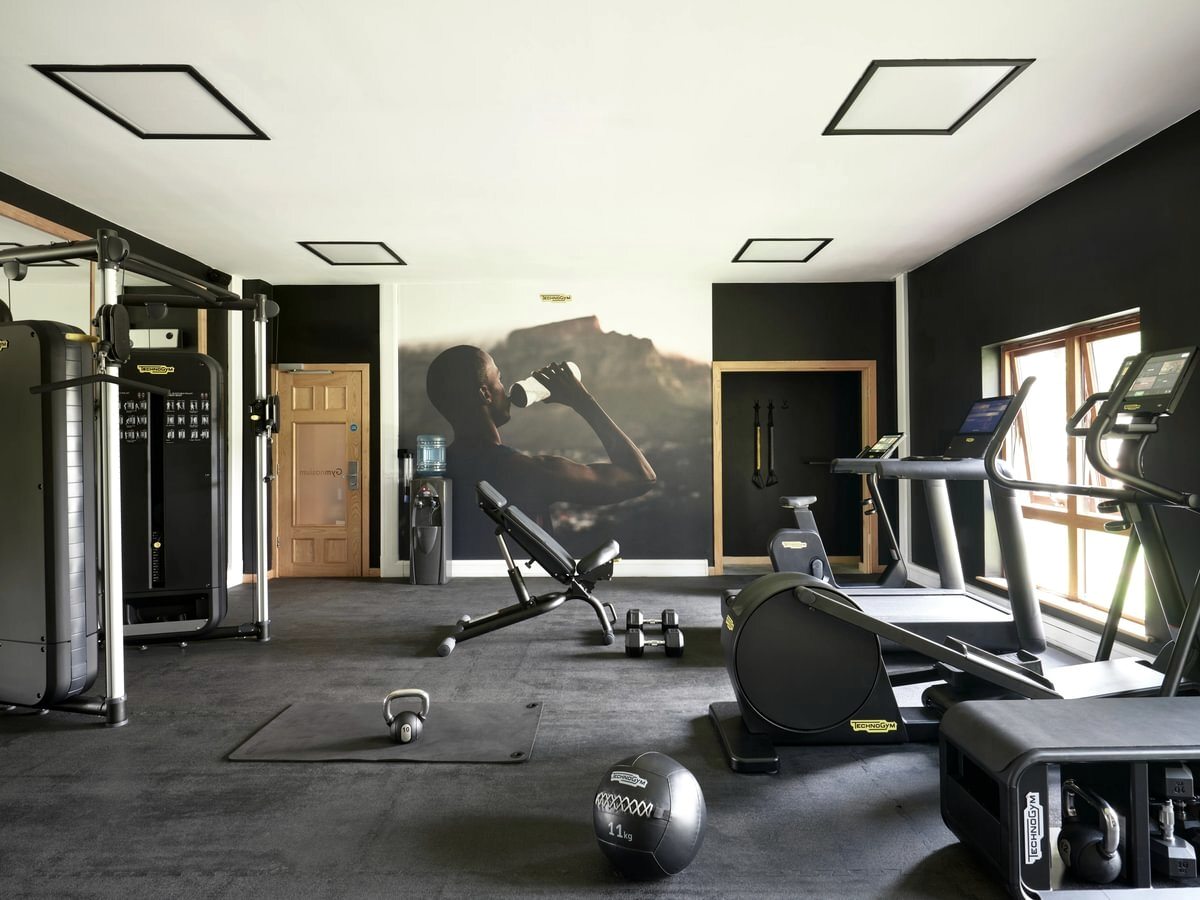 A gym with a treadmill, exercise bike, multi-gym, dumbbells, a kettlebell and a weights bench on dark rubber flooring.