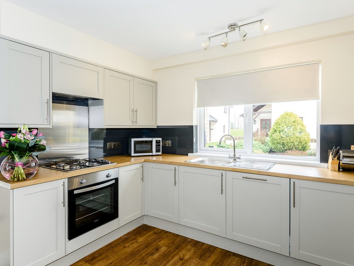 A grey Shaker kitchen with wooden worktops, a gas hob, built-in oven, microwave and a window above the sink looking onto the grounds.