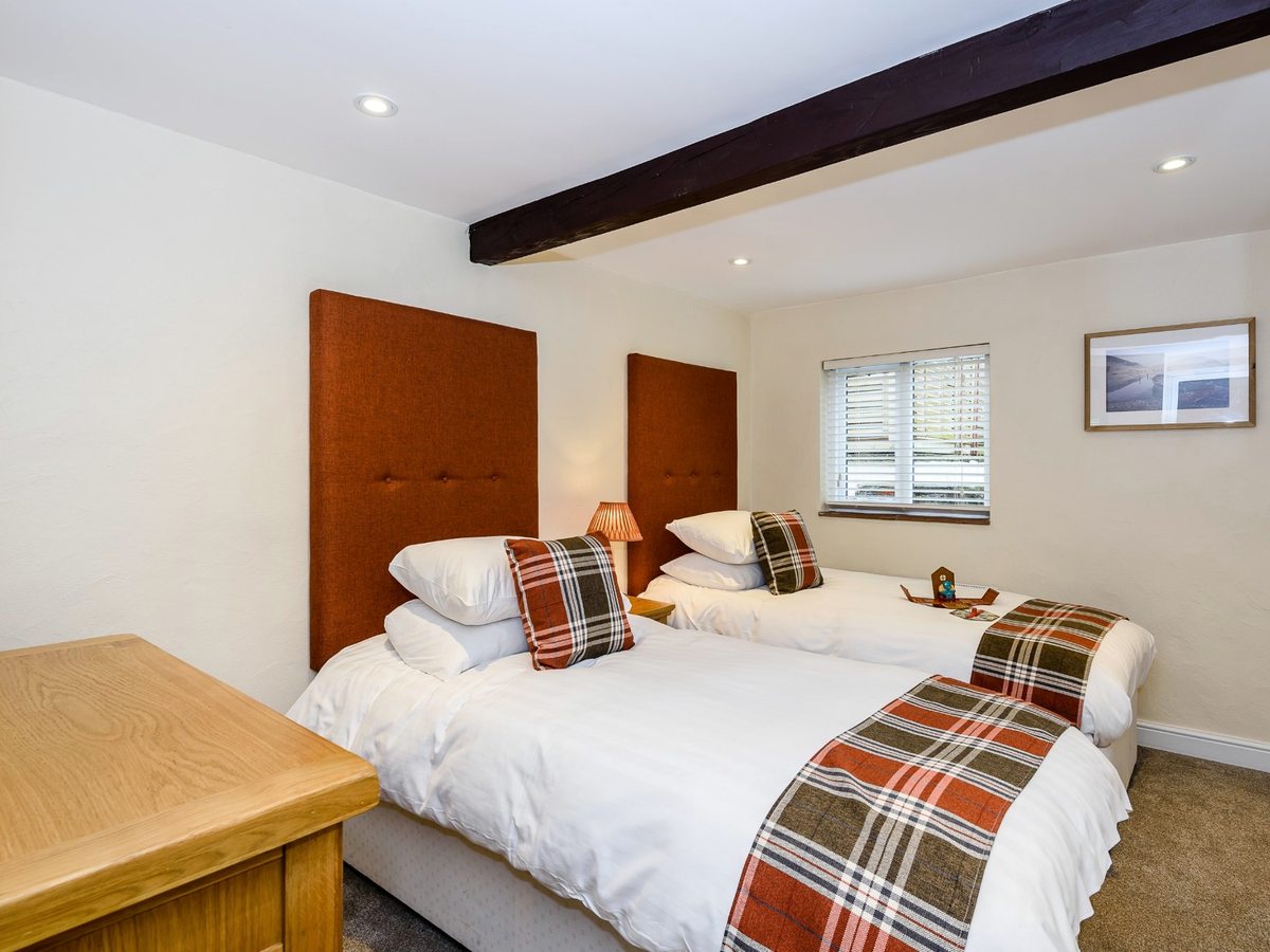 Two single beds with orange upholstered headboards and tartan runners in a white room with a dark ceiling beam and a shuttered window.